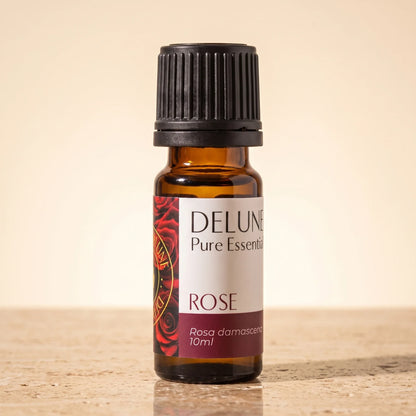Delune Rose Pure Essential Oil, 10ml amber glass bottle on warm travertine stone