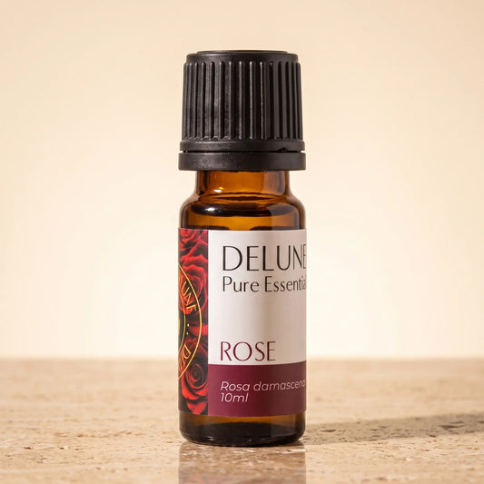 Delune Rose Pure Essential Oil, 10ml amber glass bottle on warm travertine stone